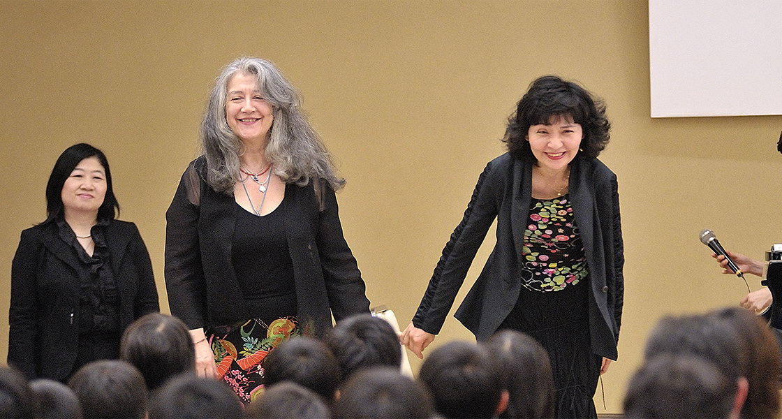 Martha Argerich (left) and Kyoko Ito (right) on a stage bowing in recognition of applause from the audience.